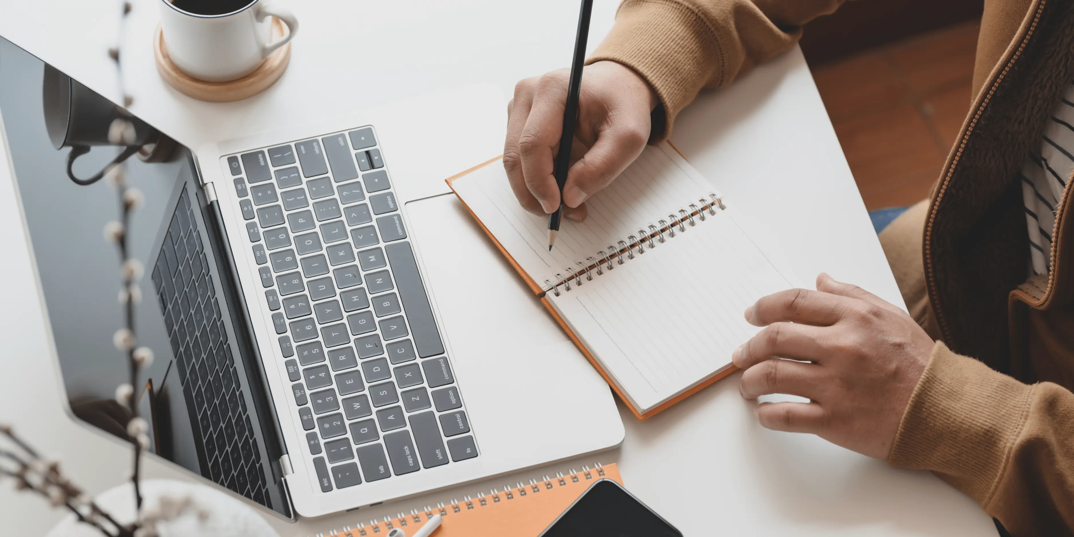 Image of a laptop and a person writing in a notebook